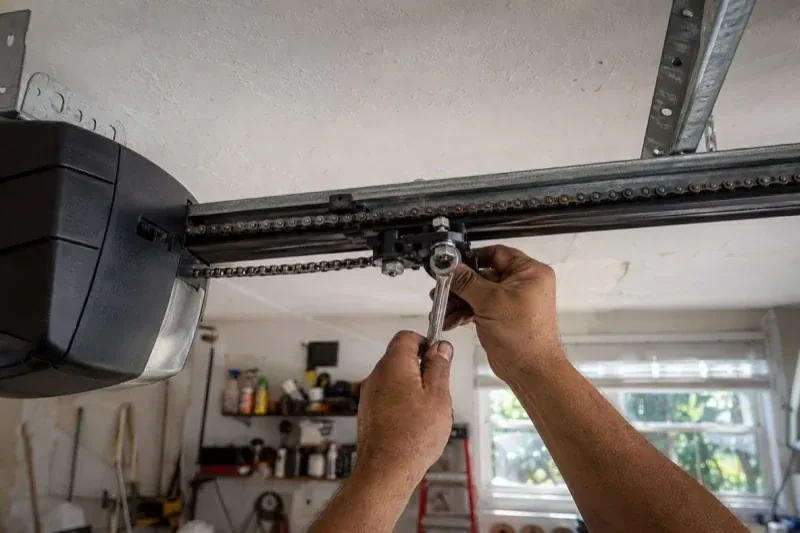 Hands holding a wrench against an opener trolley beneath a chain rail — Chain-Drive Opener Repair, Richmond Hill