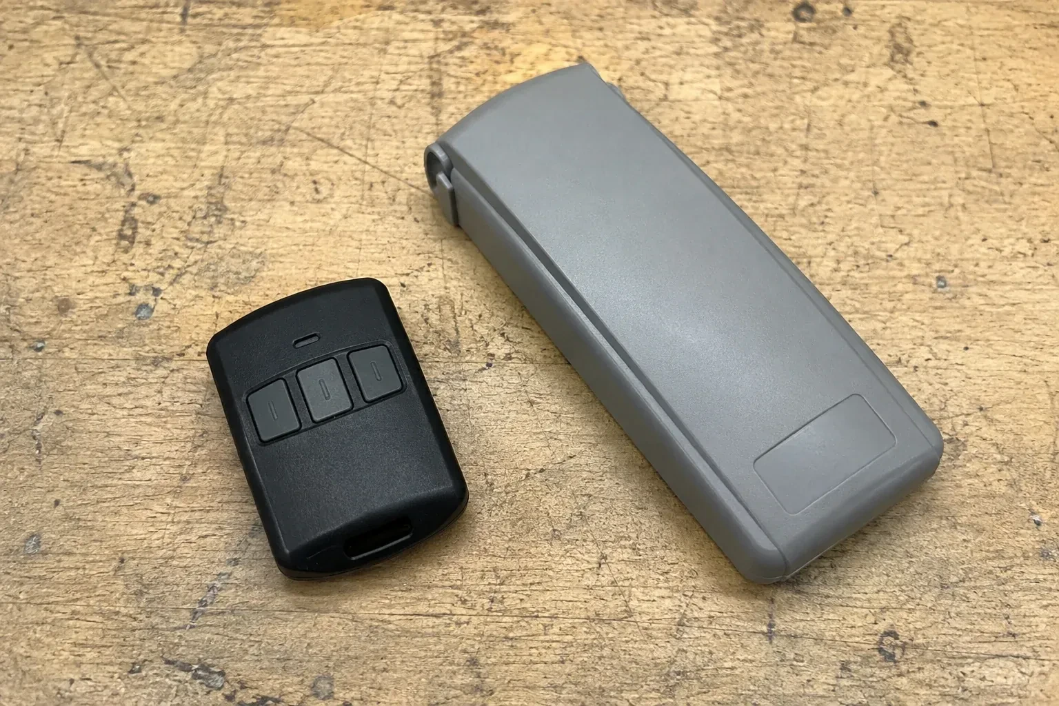 Three-button remote beside a closed grey keypad cover on a workbench. — Garage Door Remote and Keypad Programming, Richmond Hill