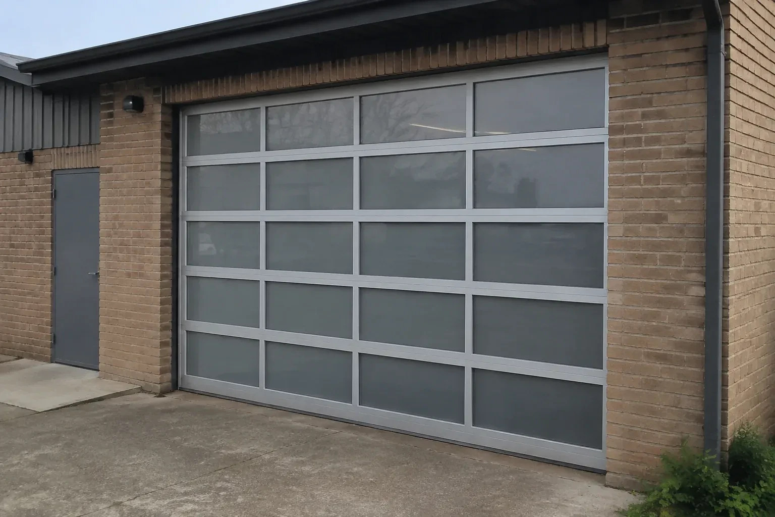 Closed glazed sectional door in a grey metal frame at a brick workshop. — Full-View Glass Garage Door Installation, Richmond Hill