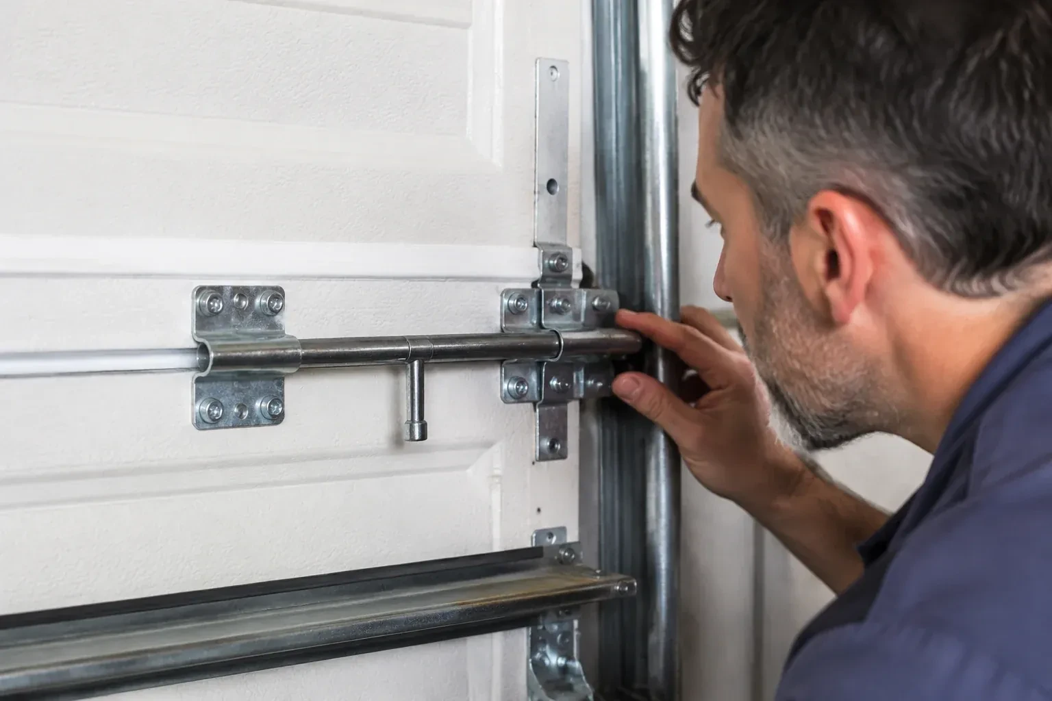 Person leaning close to a white paneled door, one hand on a metal slide-bolt bar mounted across the panel. — Garage Door Manual Lock Repair, Richmond Hill