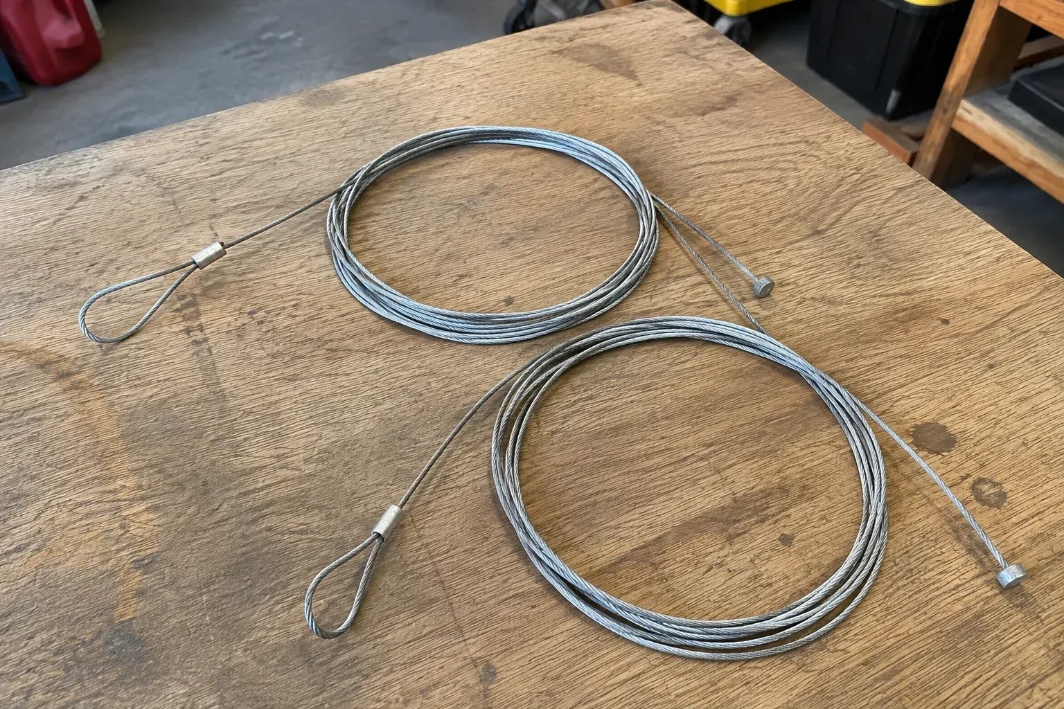 Two coiled steel cables with loop and stop ends on a workbench. — Garage Door Cable Replacement, Richmond Hill