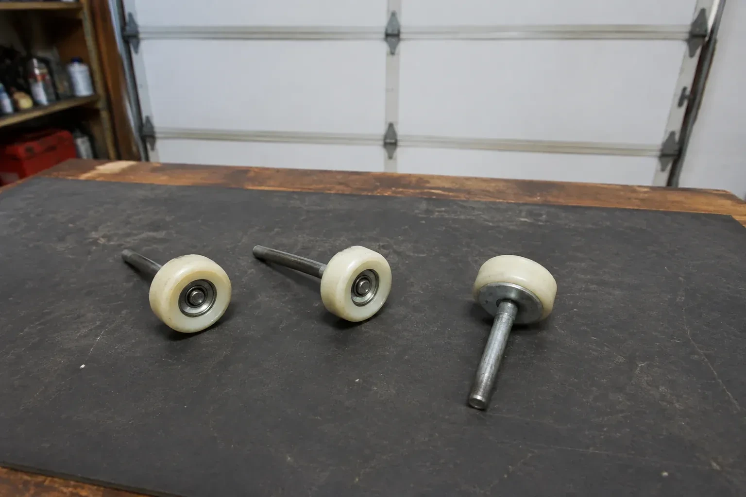 Three detached nylon-wheel garage door rollers with steel stems on a work mat. — Garage Door Roller Replacement, Richmond Hill